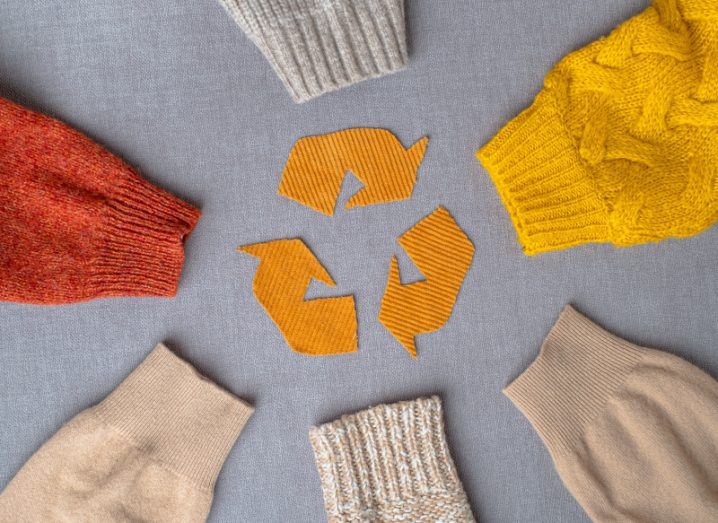 Six sleeves of woollen jumpers in muted autumnal yellow, red and brown colours in a circle around a material yellow recycling logo to represent circularity.