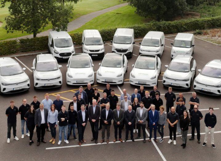 Aerial view of a group of men and women standing in a car park, with multiple white cars and vans behind them. They are part of the company ePower.