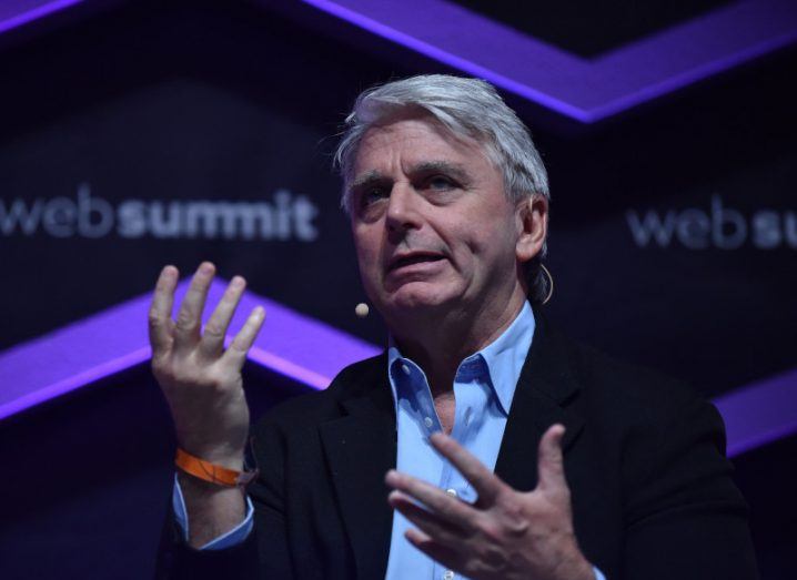 A man in a suit speaking in front of a WebSummit logo. He is John Riccitiello of Unity.