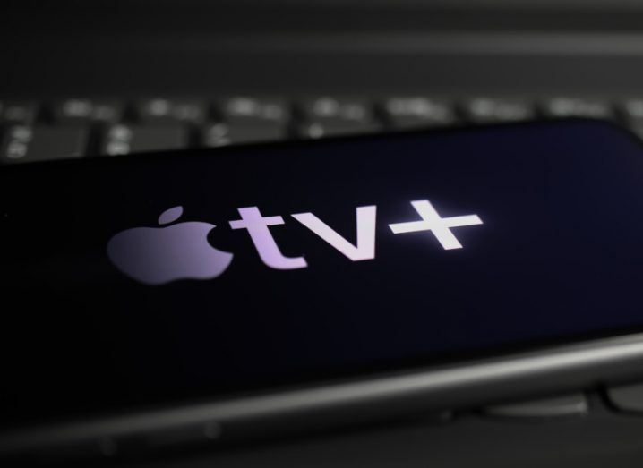 The Apple TV plus logo on a smartphone screen. The phone is laying on a keyboard.
