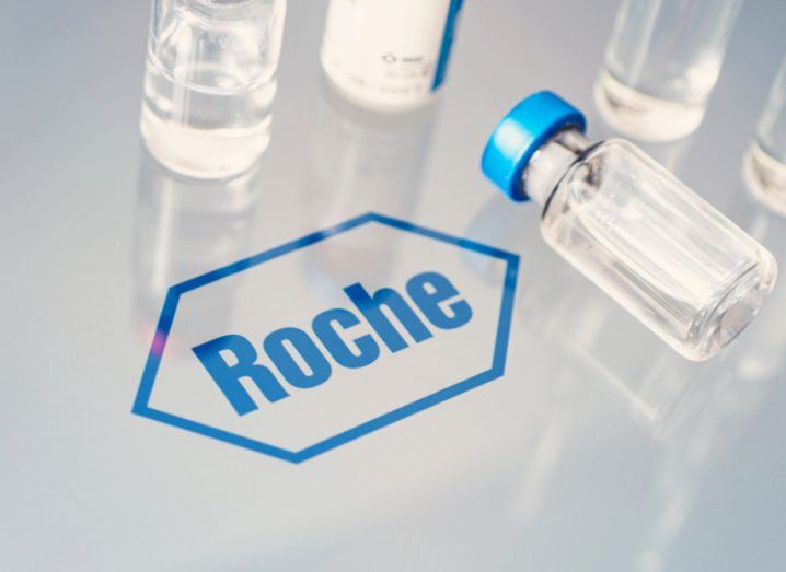 The Roche company logo on a clear surface, next to glass vials on the surface.