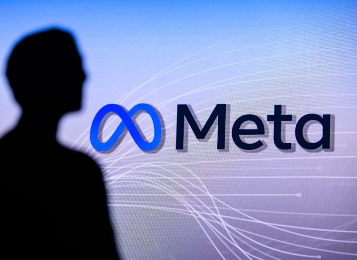 The Meta logo behind a silhouette of a man.
