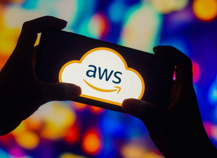 The Amazon Web Services or AWS logo on a smartphone screen. The phone is being held in a person's hands.