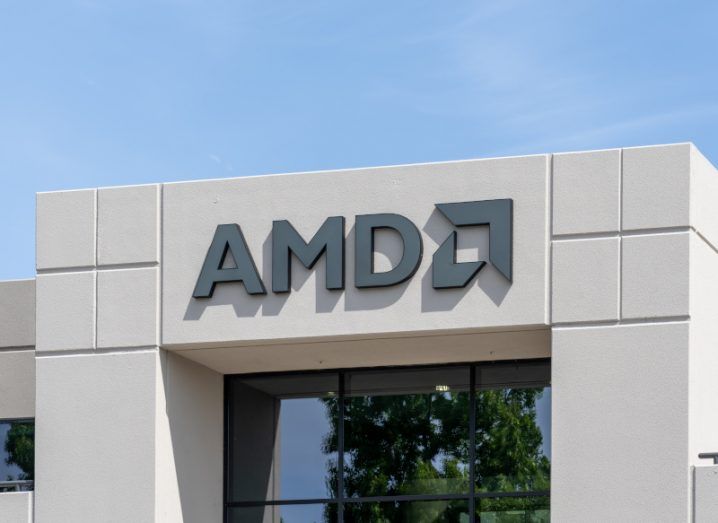The AMD logo on the front of a white building, with windows below the logo and a blue sky above it.