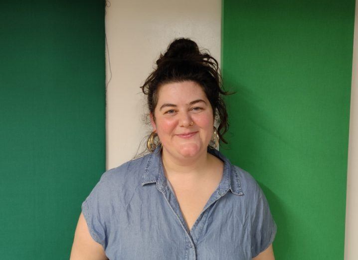 A woman stands against a green and white wall. She is Aisling Murray, director of the Beta festival.
