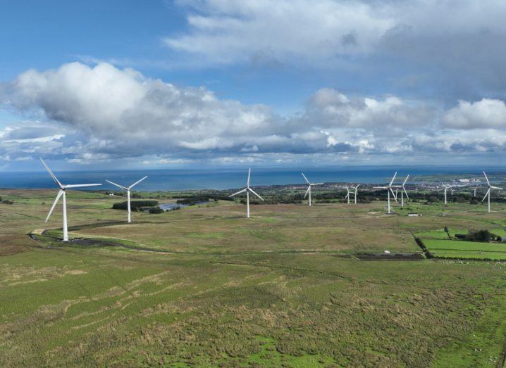 Multiple wind turbines in a green field with clouds and blue sky in the background.