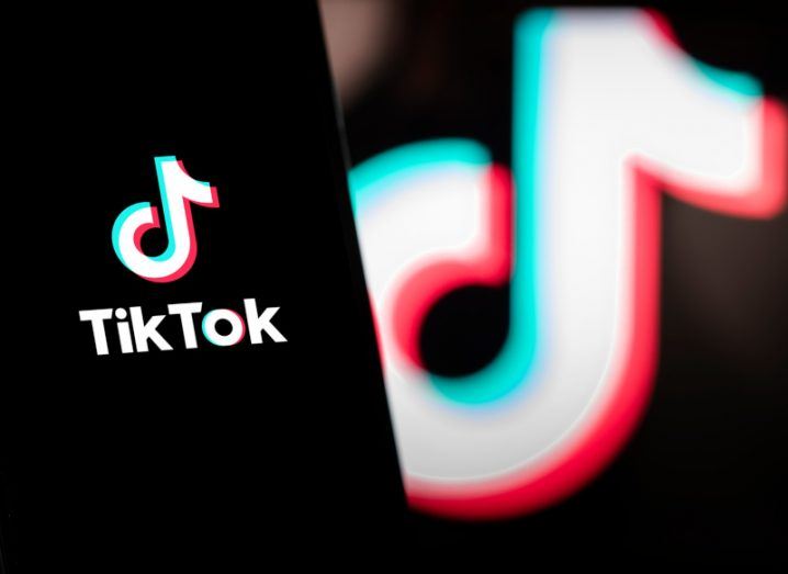 A phone with the TikTok logo on it with a larger version slightly blurred in the background.
