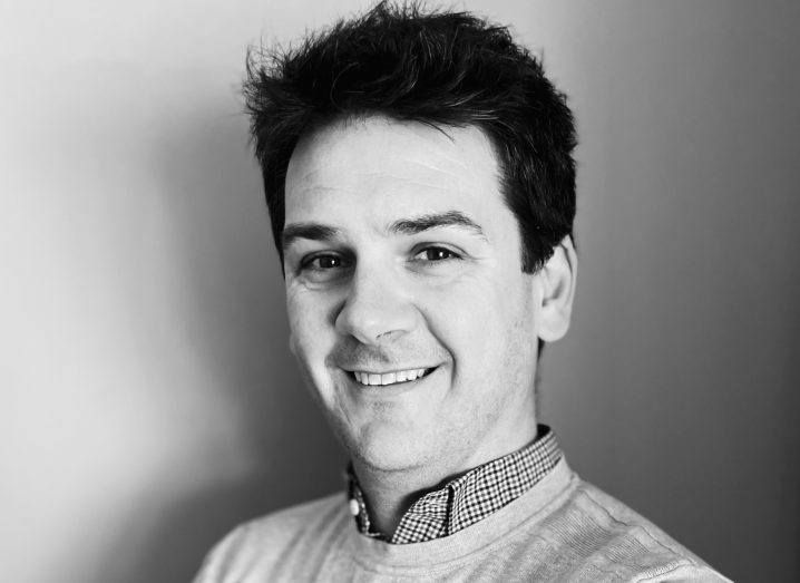 A headshot in black and white of Colm Murphy, co-founder of Gyst. He smiles at the camera and wears a short and jumper.