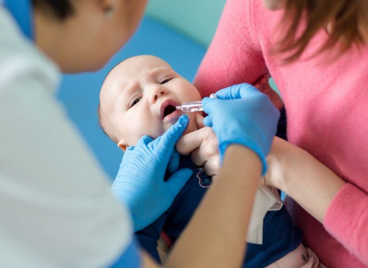 Photo of a person giving a baby an oral vaccine while a lady holds it.