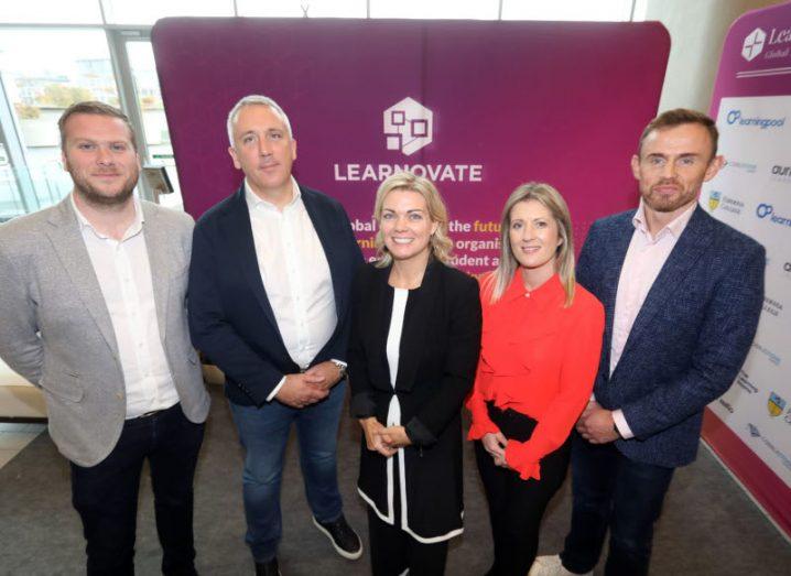 Three men and two women standing in a row in front of a sign that has the Learnovate logo on it. They are part of Learnovate and AWS.