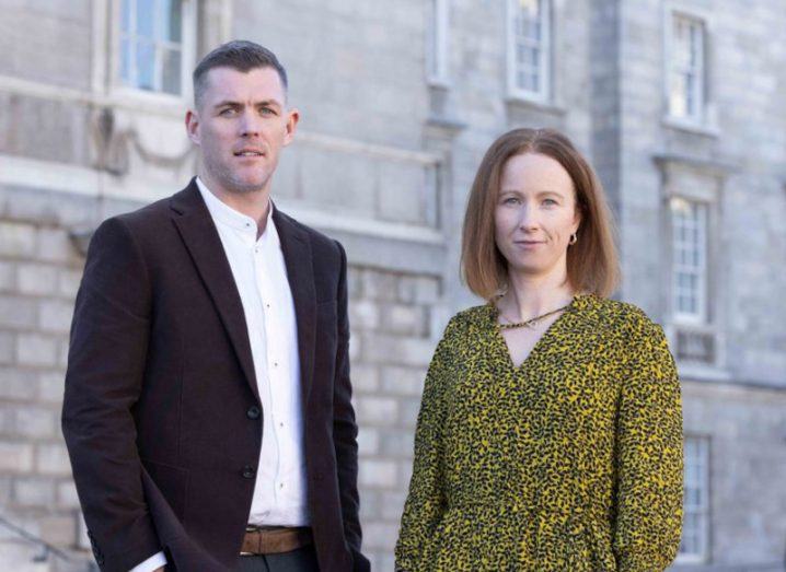 A man and a woman standing together in front of a grey building. They are from Trinity College Dublin.