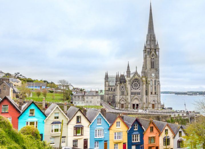 A view of Cobh town in Cork with colourful houses on a hill and a church steeple visible behind them.