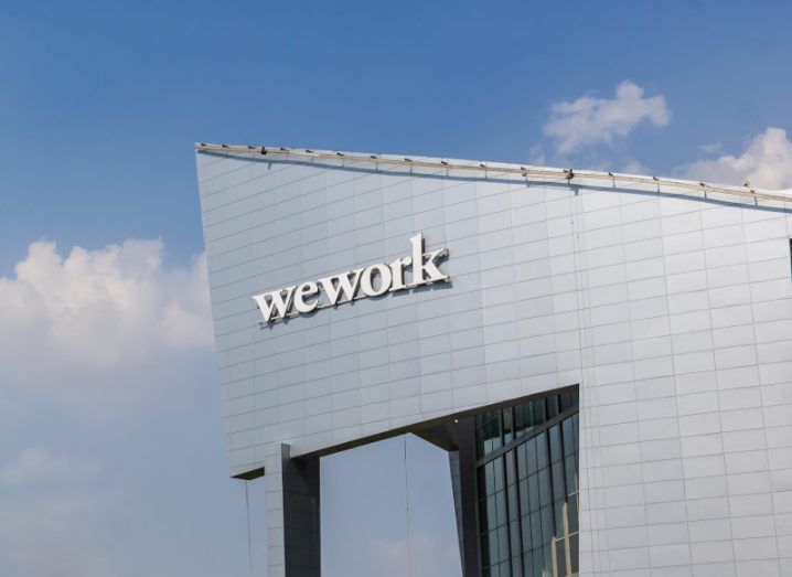 A grey building with the WeWork logo on the front and a blue sky with clouds in the background.
