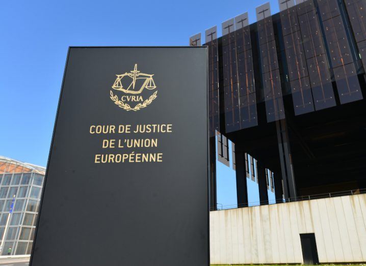 A sign of the European Court of Justice in front of a large building, with a blue sky in the background.