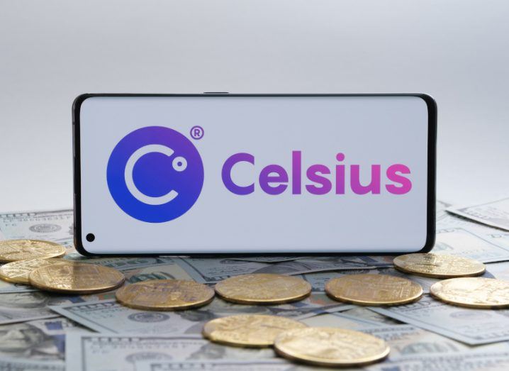 The Celsius Network logo on a smartphone screen. The phone is on top of gold coins and dollar bills.