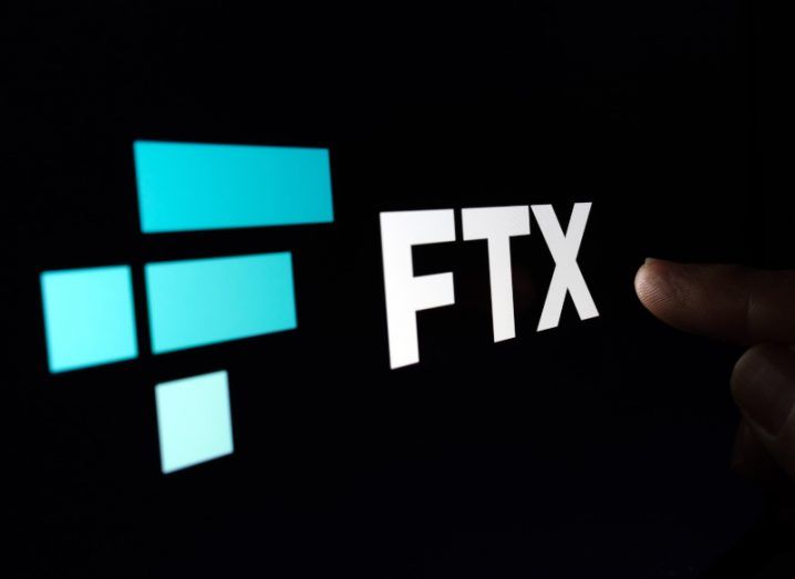 The FTX logo on a black background with a finger pointing at the logo.