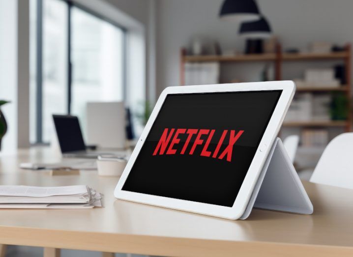 The Netflix logo on the screen of a tablet, which is on a wooden table in a room.