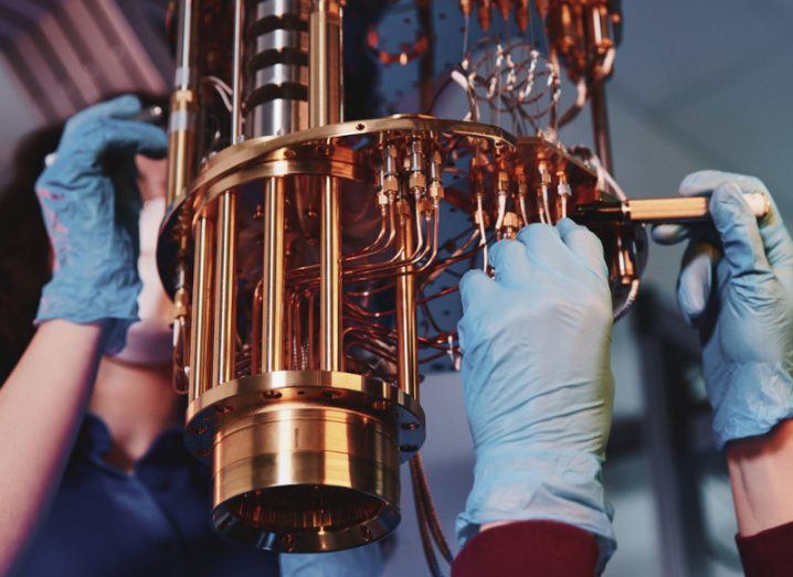 Two people wearing blue gloves and holding tools as they work on a small quantum computer.