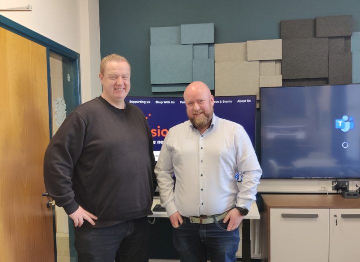 Two men standing in an office in front of two screens, with a wooden door to the side. They are Kyran O’Mahoney and Sean Doran of Vision Ireland and IA Labs.