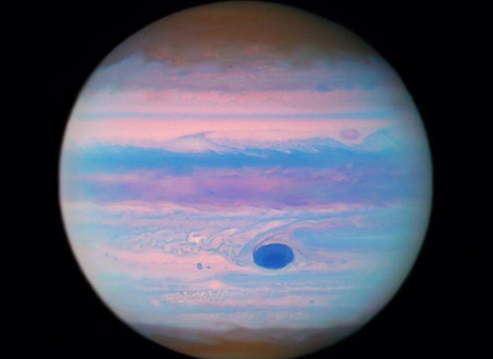 An image of Jupiter with a dark purple spot on its surface, on a black background.