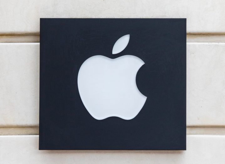 Apple logo in white on a black background. The logo is placed on what appears to be a beige coloured wall.