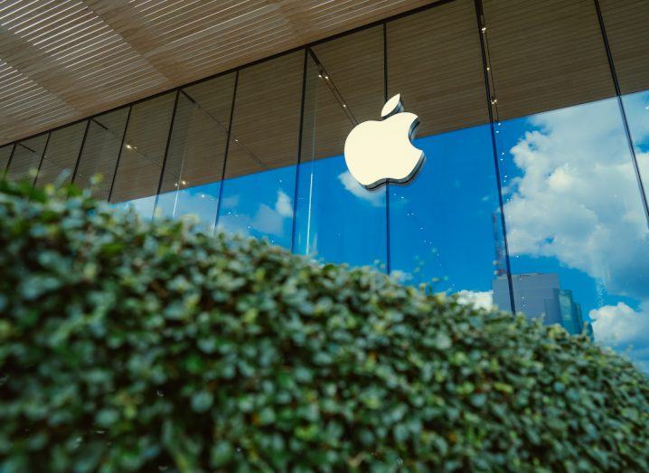 Apple logo on a building with a green bush seen in the foreground.