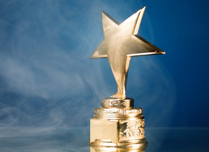 A gold star-shaped trophy stands against a blue background with smoke around it.