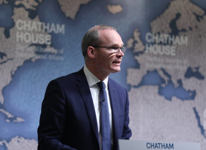 A man standing on a stage in front of a map showing parts of the world such as Europe, Africa and the Middle East. He is Simon Coveney.