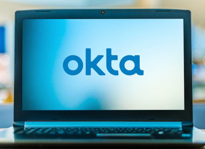 The Okta logo on a computer screen, which is on a small desk.