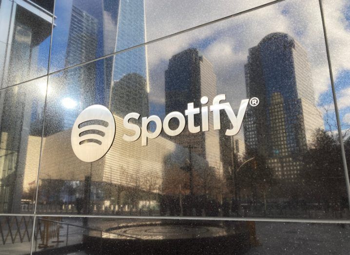 The Spotify logo on the side of a building, with a city reflecting on the building's surface.