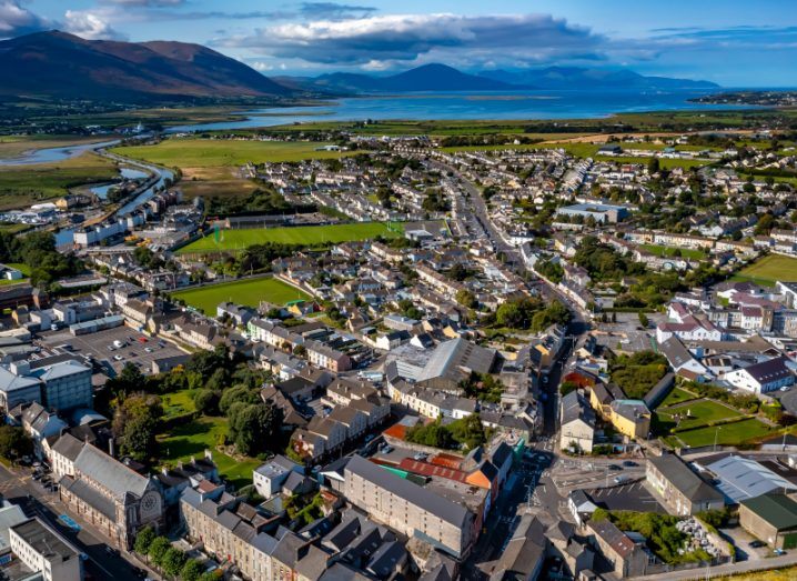 An aerial view of Tralee in county Kerry, with various buildings in the town. There are mountains and blue water in the distance.