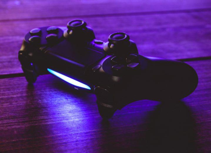 Gaming controller with a light on the back sits on a wooden floor with a purple light shining on it.
