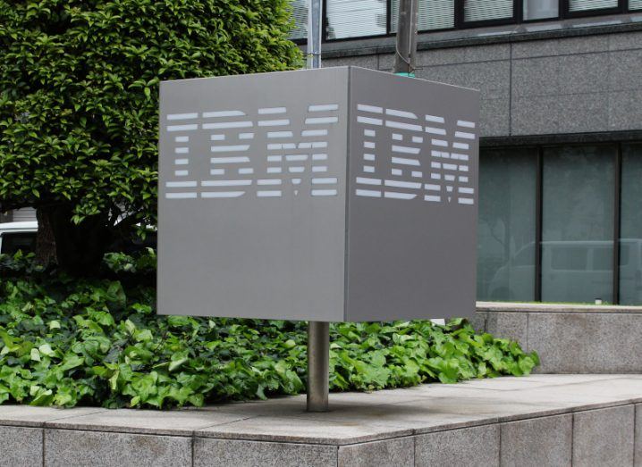 A grey cube sign with the IBM logo on it in front of a large office building.