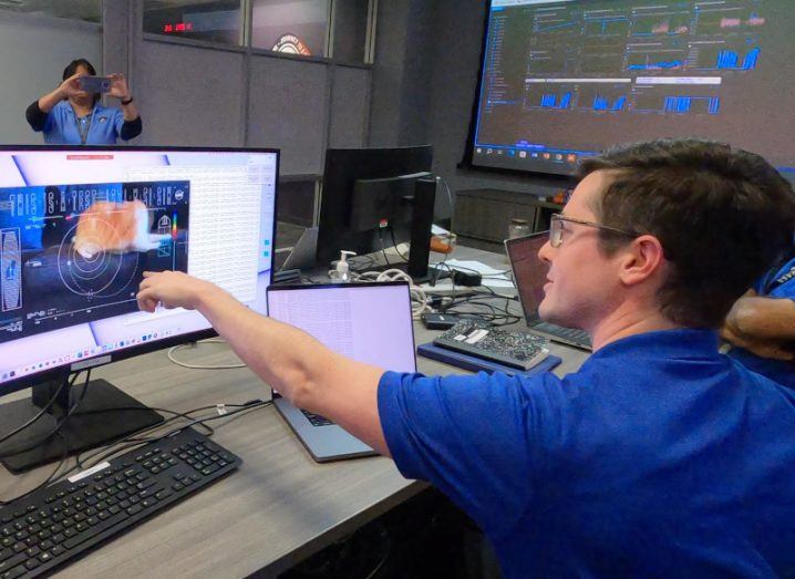 NASA workers in blue polo shirts look at a computer screen with a cat video on it.