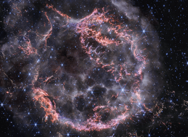 Image of a supernova remnant in space, showing a circle of gas and blue stars visible deeper in the image.