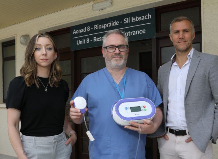 Two men and a woman standing together. The man in the middle is holding a device from SymPhysis Medical.