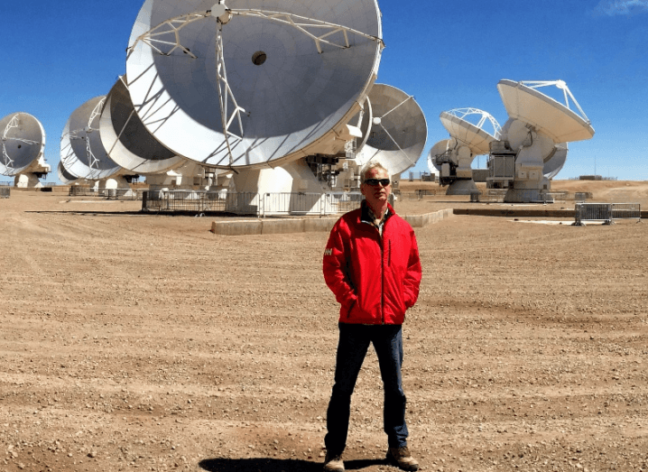 A man standing in front of multiple ground satellites in a desert. He is Professor Tom Ray of DIAS.