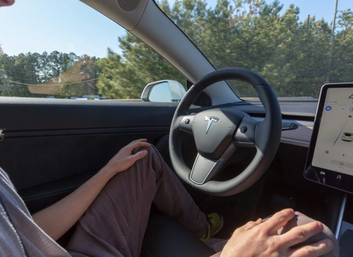 Man sitting in front of the steering wheel of a Tesla car.