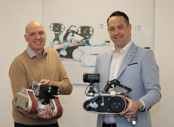 Two men pose for a photo with robots made by Invert Robotics in their hands.