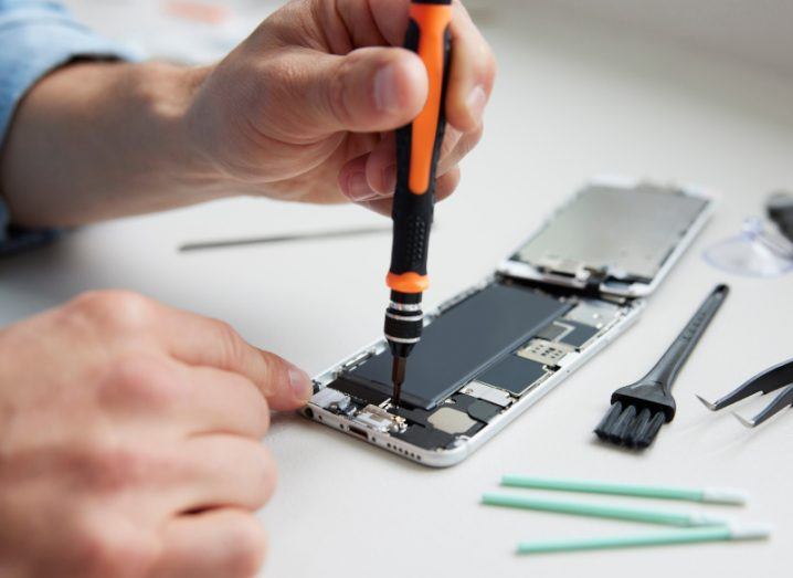 A close-up of a man with a repair kit trying to fix a smartphone.