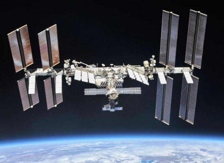 Image of the International Space Station or the ISS in orbit, with the darkness of space in the background and the Earth visible below it.
