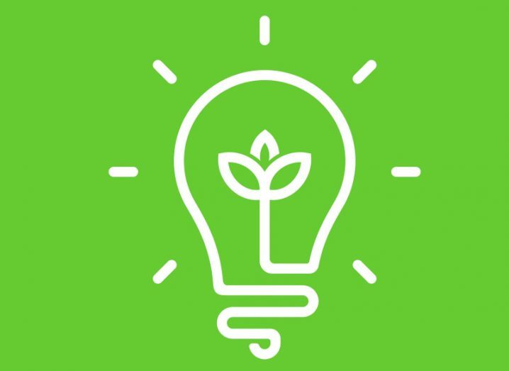 A white cartoon drawing of a lightbulb with a plant in the middle against a green background, symbolising tech sustainability.