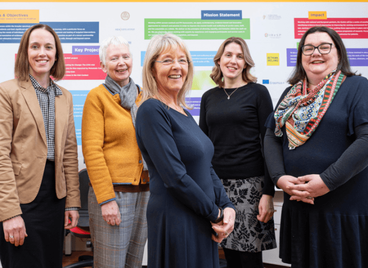 Five women from UCC smile at the camera in front of UCC marketing materials.