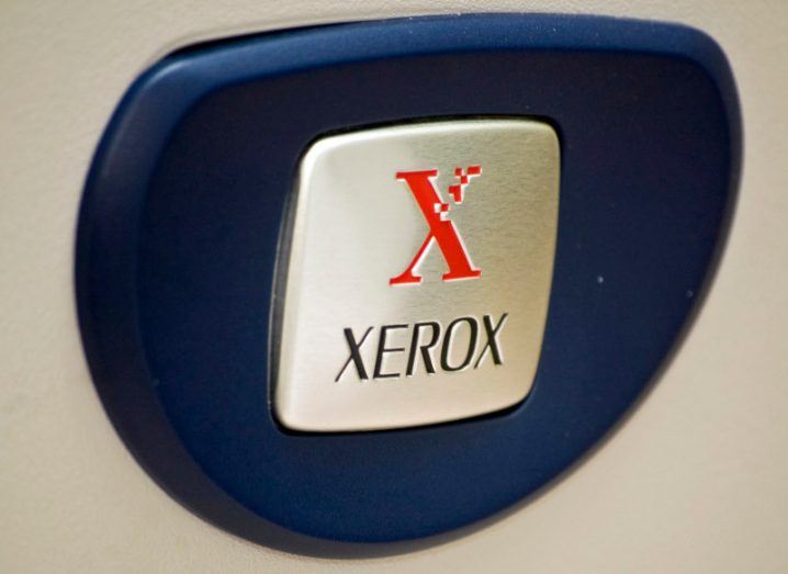 The Xerox company logo on a grey square, with a dark blue piece of material around it.