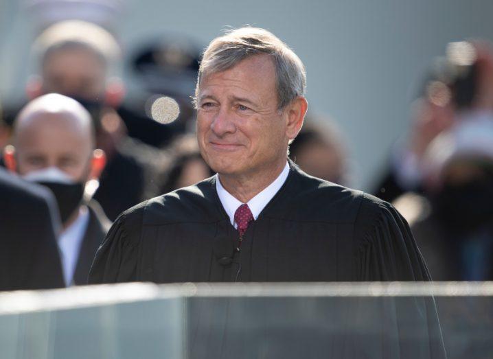 A man standing in a crowd, wearing a black outfit. He is US chief justice John Roberts.