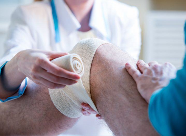 A patient getting a bandage removed from their knee with the help of a doctor.