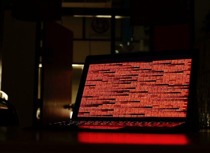 A computer in a dark room with lines of red code on the screen.