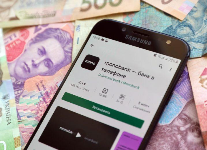 A mobile phone with the Monobank app on the screen and various currency notes under the phone.