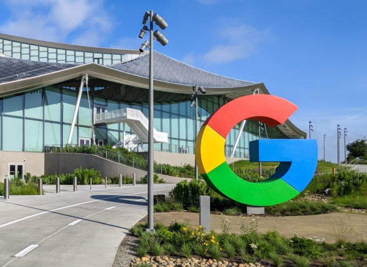 A Google logo next to a small road leading to a building, with a blue sky in the background.