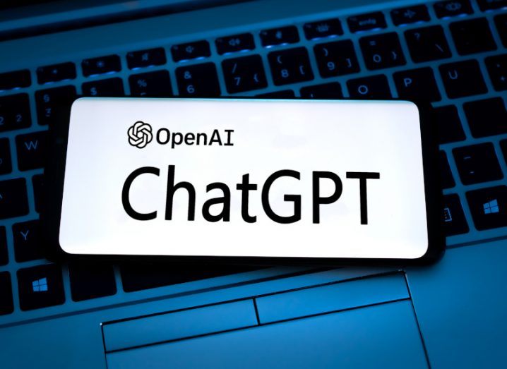 The OpenAI and ChatGPT logo on a smartphone screen. The phone is on top of a computer keyboard.